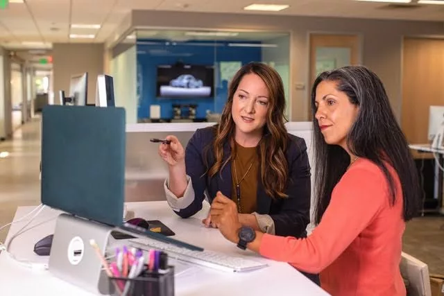 Two professional women discuss something while looking at a laptop